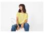 Frau in gelbem T-Shirt und blauen Jeans, sitzt auf einem weißen Stuhl.