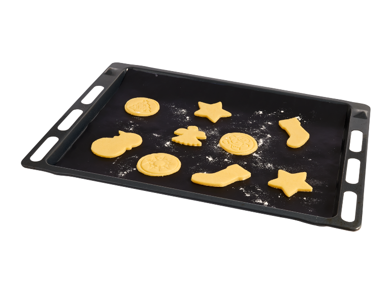 Schwarzes Backblech mit rohen Weihnachtsplätzchen in verschiedenen Formen.