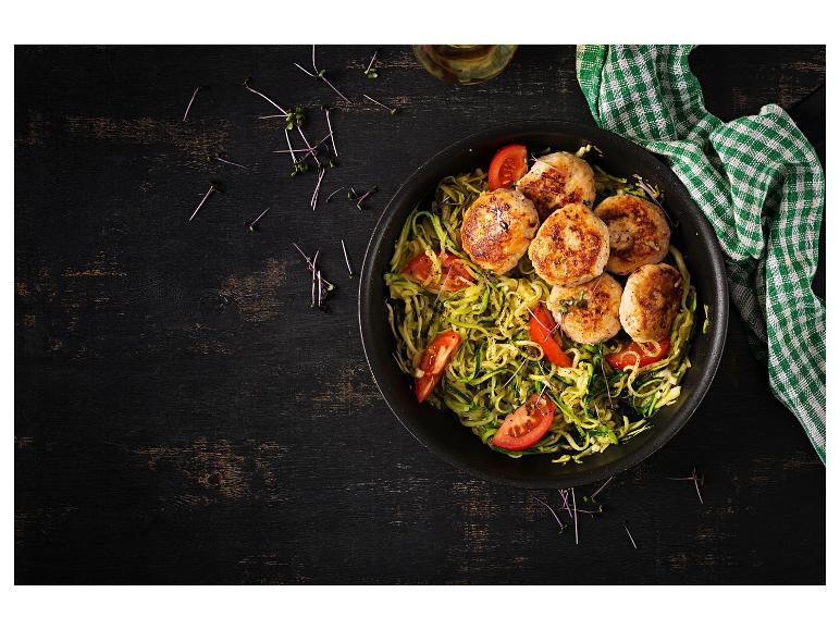 Hähnchenfrikadellen mit Zucchini-Nudeln und Tomaten in einer schwarzen Pfanne.