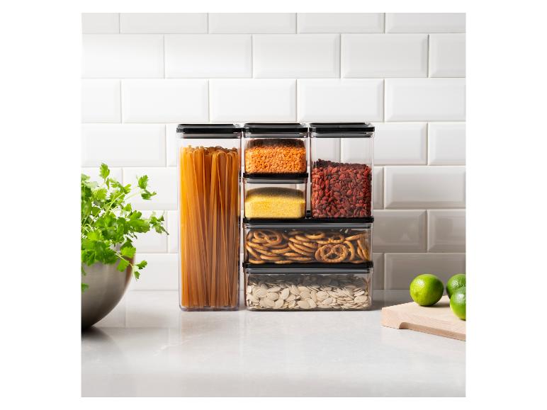 Küchenarbeitsplatte mit stapelbaren Behältern voller Trockenwaren, frischer Kräuter und Limetten.