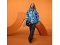 Eine Frau in blauer Skijacke und schwarzer Hose hält ein Snowboard.