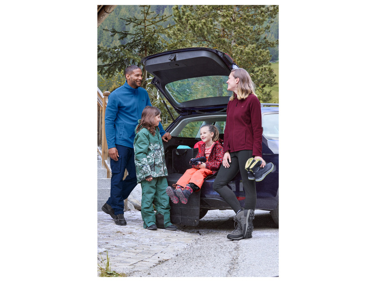 Eine Familie mit Fleecejacken und Wanderschuhen steht an einem Auto.