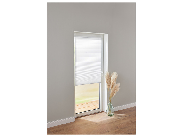 Ein weißer Plissee-Vorhang an einer Tür mit einer Vase mit Pampasgras.