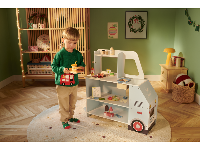 Junge in grünem Pullover mit Spielzeug-Imbisswagen und Weihnachtsdekoration.