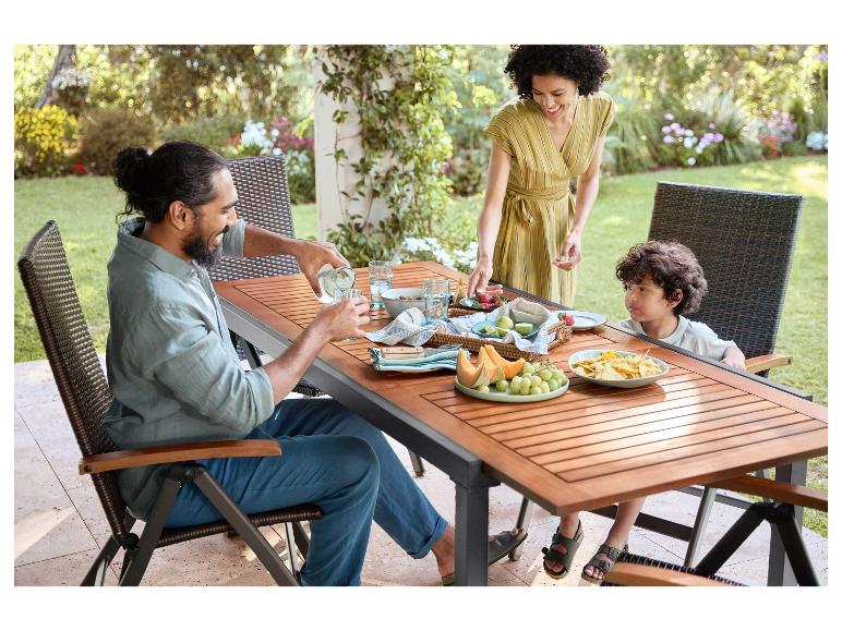 Familie genießt ein Essen im Freien mit Holztisch, Stühlen und frischem Obst.
