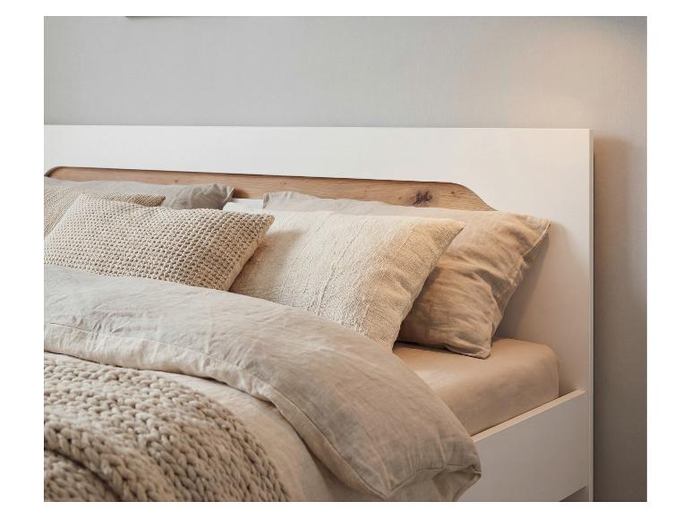 Bett mit Holzkopfteil und beiger Bettwäsche mit Kissen unterschiedlicher Texturen.