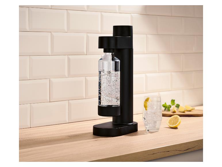 Schwarzer Sprudelbereiter mit sprudelnder Flasche, einem Glas und Zitronen.