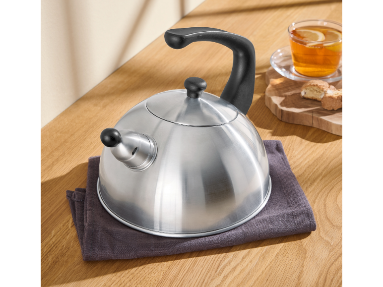 Edelstahl-Pfeifkessel auf einer Holzoberfläche mit einer Tasse Tee und Keksen.