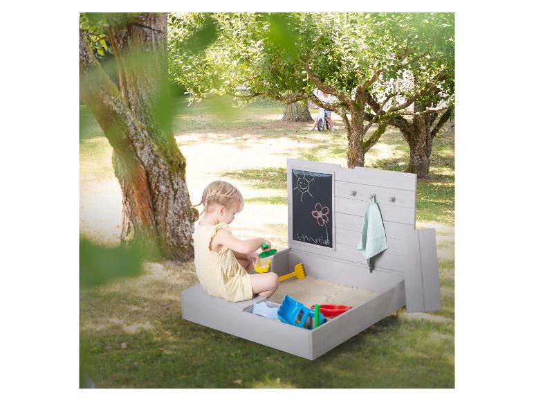 Mädchen spielt in einem Holzsandkasten mit Kreidetafel und Sandspielzeug.
