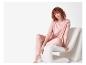 Rothaarige Frau in rosa Pyjama sitzt auf einem weißen Stuhl.