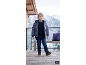 Kleiner Junge in Winterjacke, Pullover, Jeans und Stiefeln auf einer verschneiten Terrasse.
