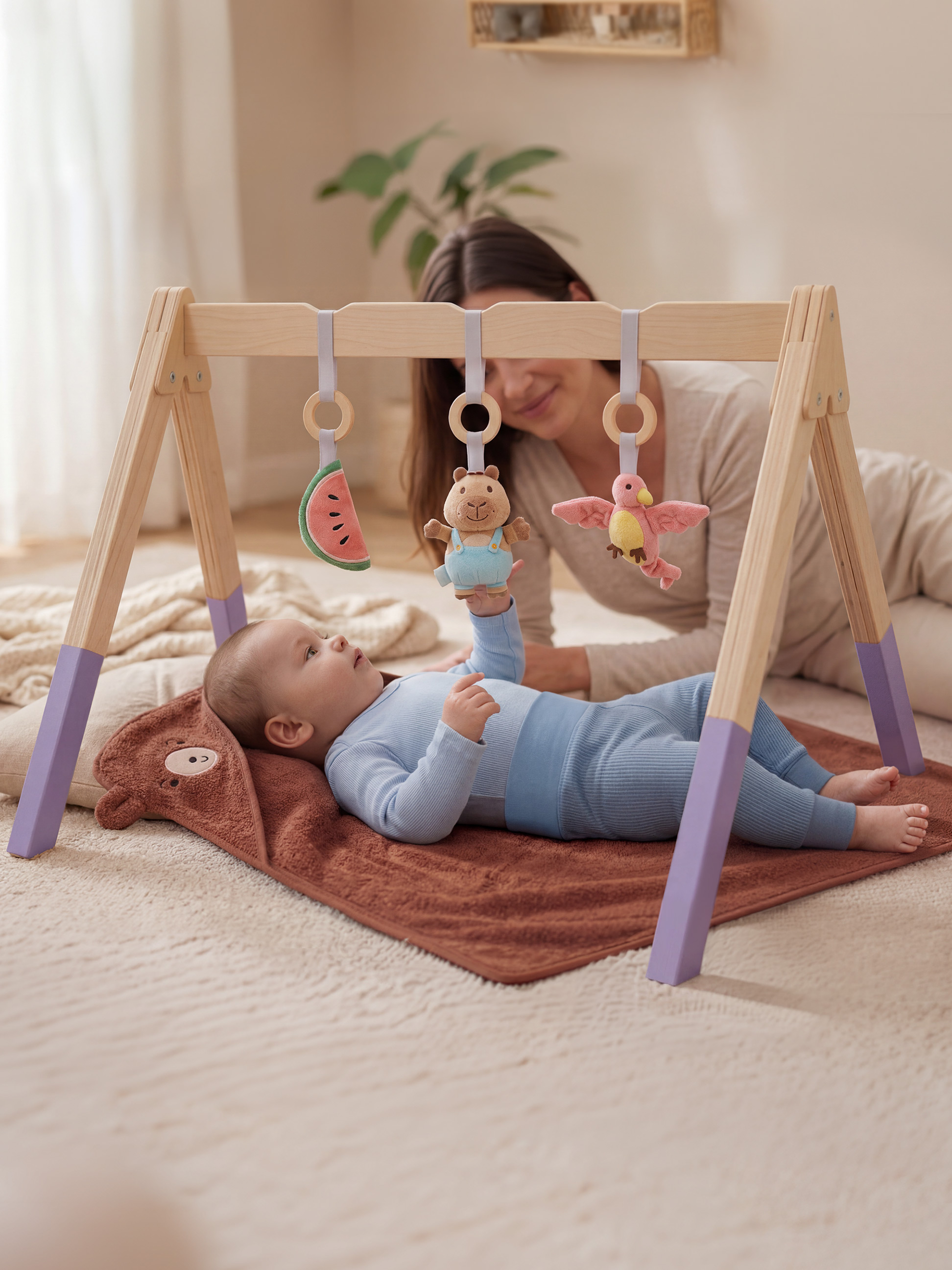Baby spielt mit einem Holzspielbogen mit Hängespielzeug, Mutter im Hintergrund.