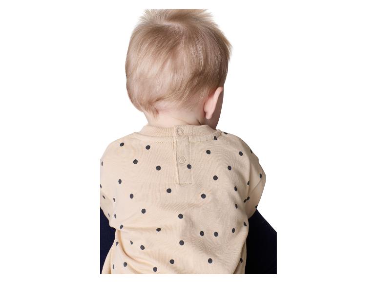 Rücken eines Babys in einem beigen gepunkteten Hemd, mit Knöpfen am Hals.