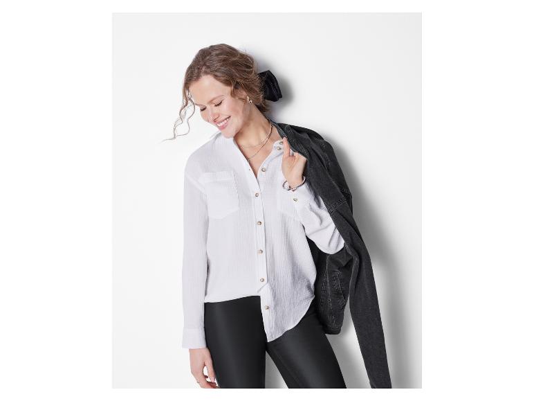 Frau in weißem Hemd, schwarzen Leggings und schwarzer Jeansjacke, lächelnd.