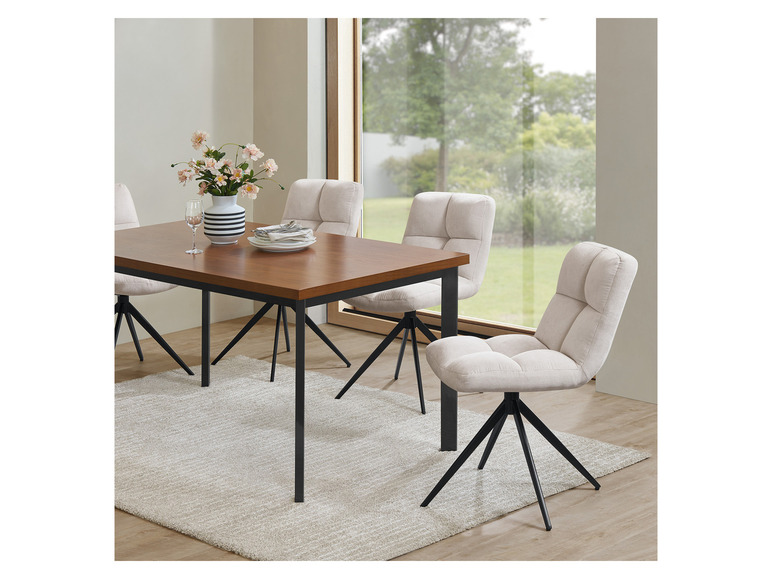 Ein Esstisch aus Holz mit vier beigefarbenen Stühlen mit schwarzen Beinen.