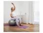 Schwangere Frau sitzt auf einem Gymnastikball auf einer Yogamatte und dehnt sich.