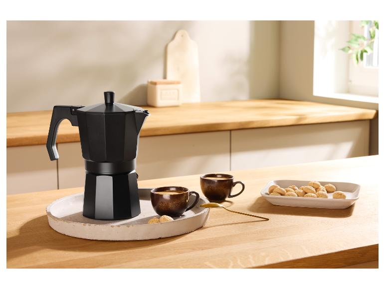 Schwarze Kaffeemaschine, zwei Tassen Kaffee und Kekse auf einem Holztisch.