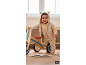 Lächelndes Baby in Strampler und Strickjacke mit Hase, neben einem Holzfahrrad.