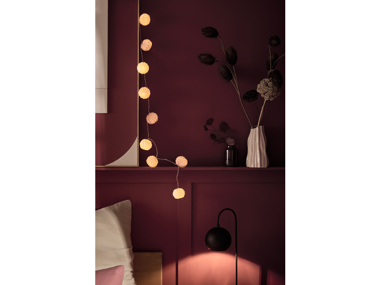 Lichterkette und Trockenblumen auf einem Regal in einem gemütlichen Schlafzimmer mit Nachttischlampe.