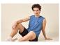 Junger Mann in blauem ärmellosem Shirt mit „SURFING VIBE“-Aufdruck und schwarzen Shorts.