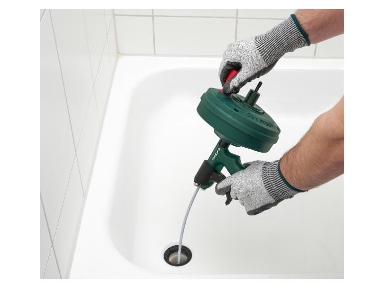 Mann mit Handschuhen benutzt einen manuellen Abflussreiniger in einer Badewanne.