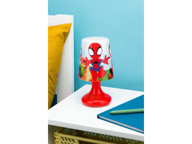 Tischlampe mit Zeichentrickfigur, blaues Notizbuch und grüner Stift auf einem weißen Tisch.
