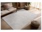 Modernes Wohnzimmer mit beigem Sofa, hellgrauem Teppich mit geometrischen Mustern und geflochtenem Pouf.