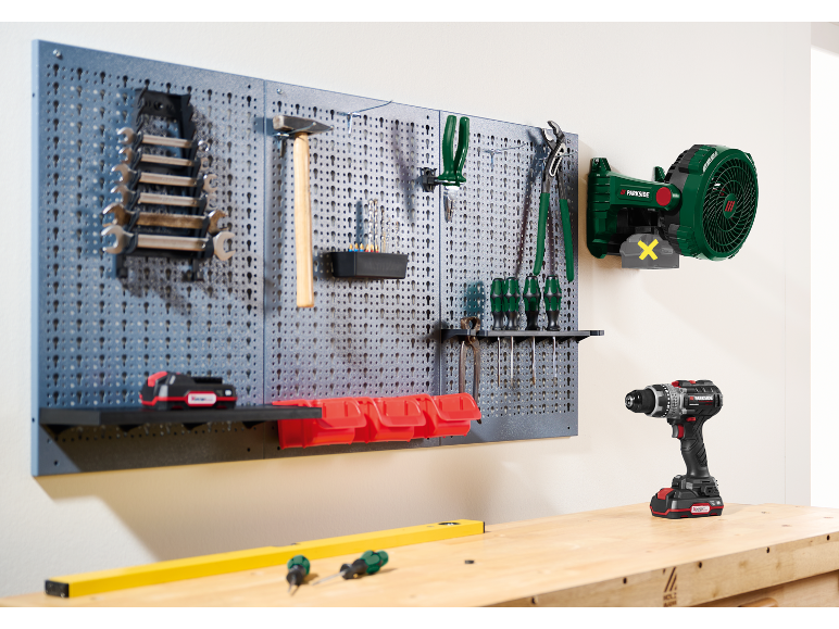 Lochwand mit Werkstattwerkzeugen, darunter Schraubenschlüssel, Hammer, Schraubendreher und Akkubohrer.