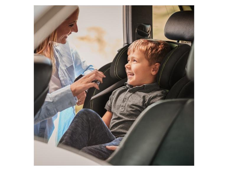Eine lächelnde Frau sichert ein Kind in einem Kindersitz.