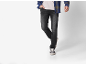 Mann trägt ein blaues Karohemd, helles T-Shirt, dunkle Jeans und Sneaker.