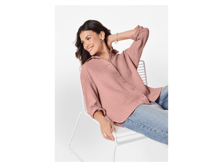 Lächelnde Frau in rosa Hemd und Jeans sitzt auf einem weißen Stuhl.