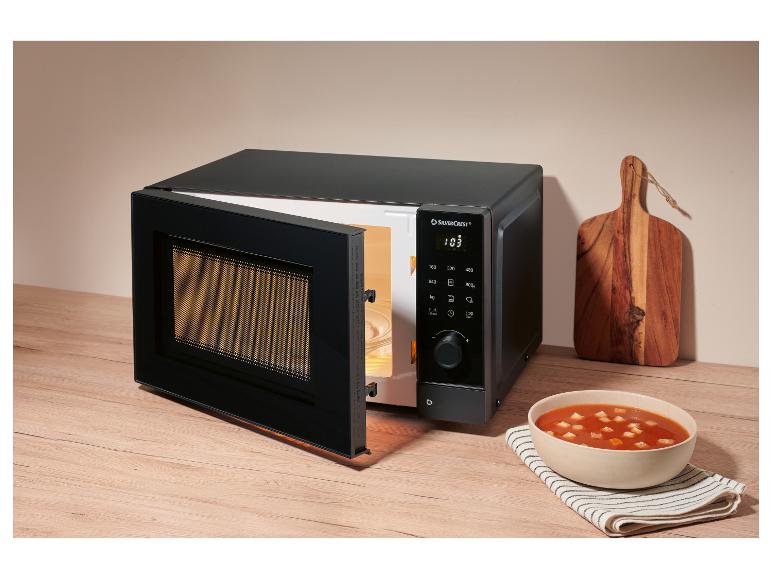 Schwarze Mikrowelle mit offener Tür und eine Schüssel Suppe auf einer Holztheke.