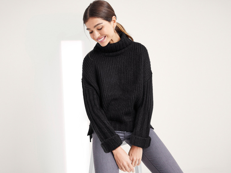 Eine Frau trägt einen schwarzen Rollkragenpullover und graue Jeans.