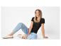 Frau in schwarzem T-Shirt und hellblauen Jeans, auf dem Boden sitzend, lächelnd.