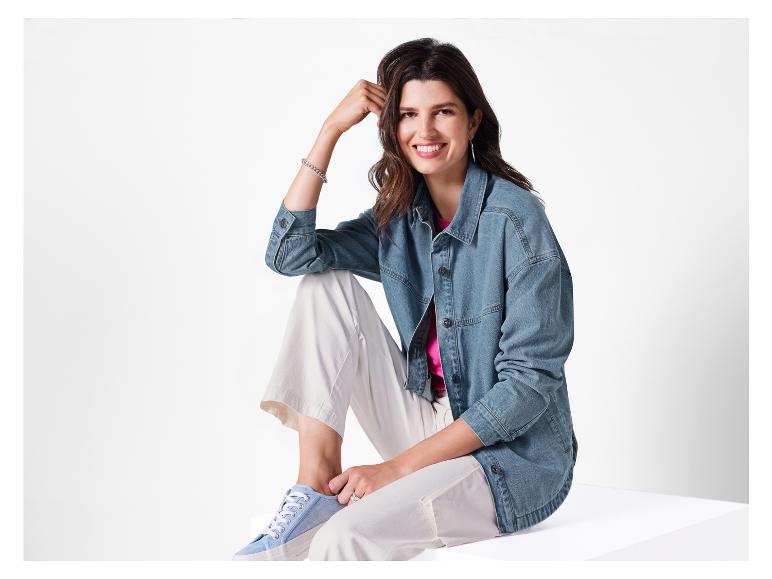 Eine Frau trägt eine Jeansjacke, weiße Hose und blaue Sneaker.