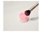 Eine pinke Make-up-Pinselreinigungsmatte mit einem Make-up-Pinsel darauf.