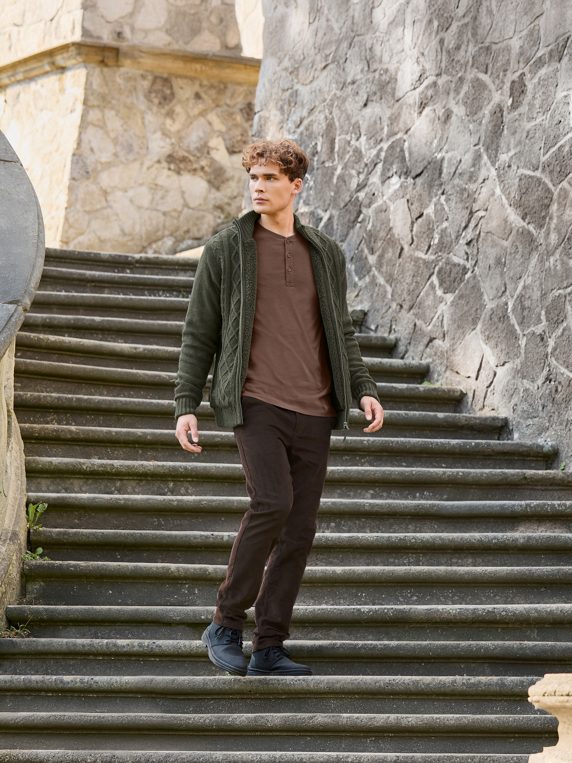 Mann in grüner Strickjacke, braunem T-Shirt und brauner Hose geht Steintreppe hinunter.