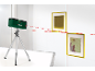 Laserwasserwaage auf Stativ, die rote Linien auf eine Wand mit zwei Bildern projiziert.