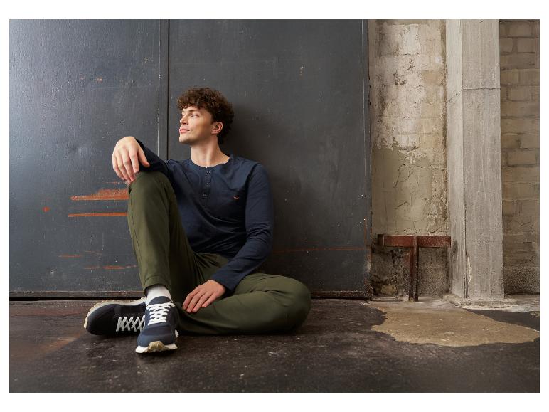 Mann in dunkelblauem Langarmshirt und grüner Hose, auf dem Boden sitzend.