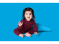 Glückliches Baby in weinrotem Rippenpyjama, sitzt auf blauem Hintergrund.