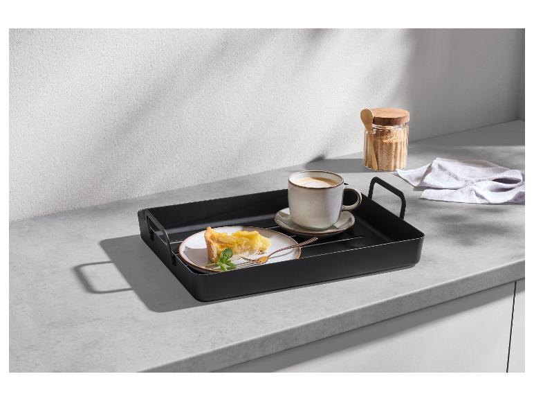 Schwarzes Tablett mit Kaffeetasse und Kuchenstück auf einer Küchenarbeitsplatte.