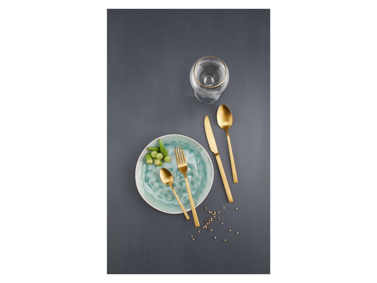 Goldenes Besteck, ein Teller und ein Glas auf einem grauen Hintergrund.