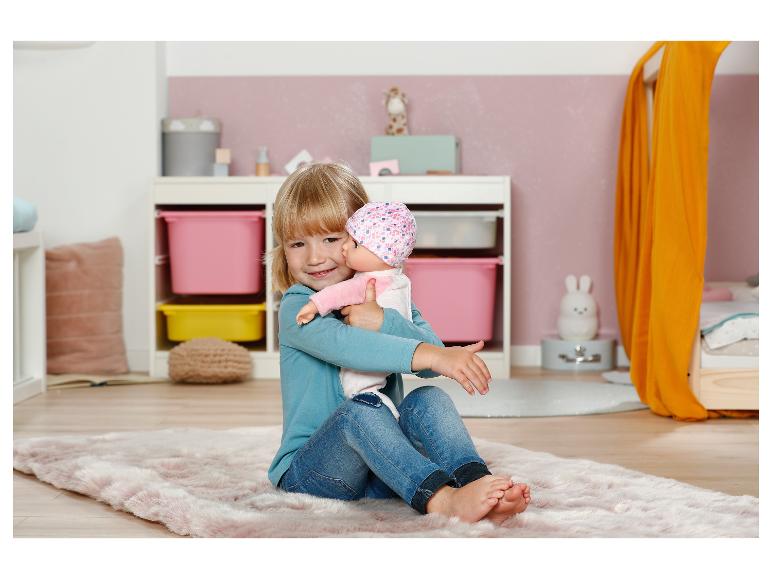 Lächelndes Mädchen mit einer Baby Annabell Puppe in einem Kinderzimmer mit rosa Teppich.