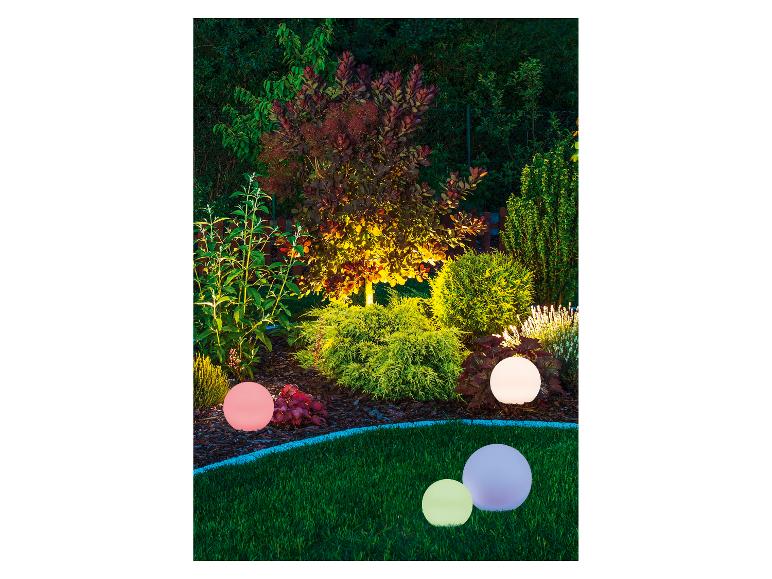 Garten mit dekorativen Kugelleuchten in verschiedenen Farben, die Sträucher und Bäume beleuchten.