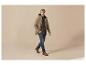 Mann in beiger Jacke, kariertem Hemd und Jeans geht.
