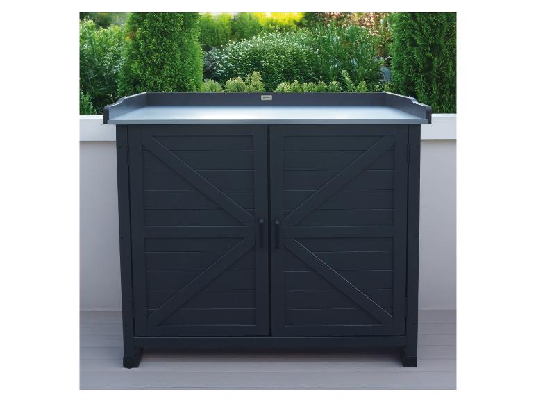 Dunkelgrauer Gartenschrank mit zwei Türen und heller Arbeitsplatte, umgeben von grünen Pflanzen.