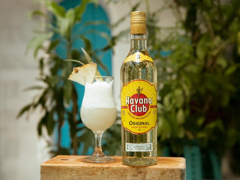 Rumflasche und Cocktail mit Ananasgarnitur auf Holzfläche, mit üppigem grünen Hintergrund.