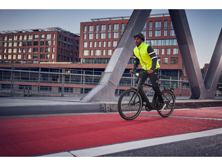 Mann in Radjacke und Helm fährt E-Bike auf rotem Radweg.