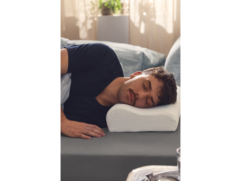 Mann schläft auf der Seite auf grauer Bettwäsche, mit dem Kopf auf einem ergonomischen Kissen.