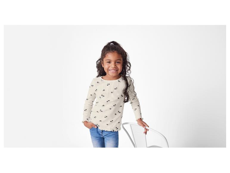 Mädchen in cremefarbenem Shirt mit Palmenprint und blauer Jeans.